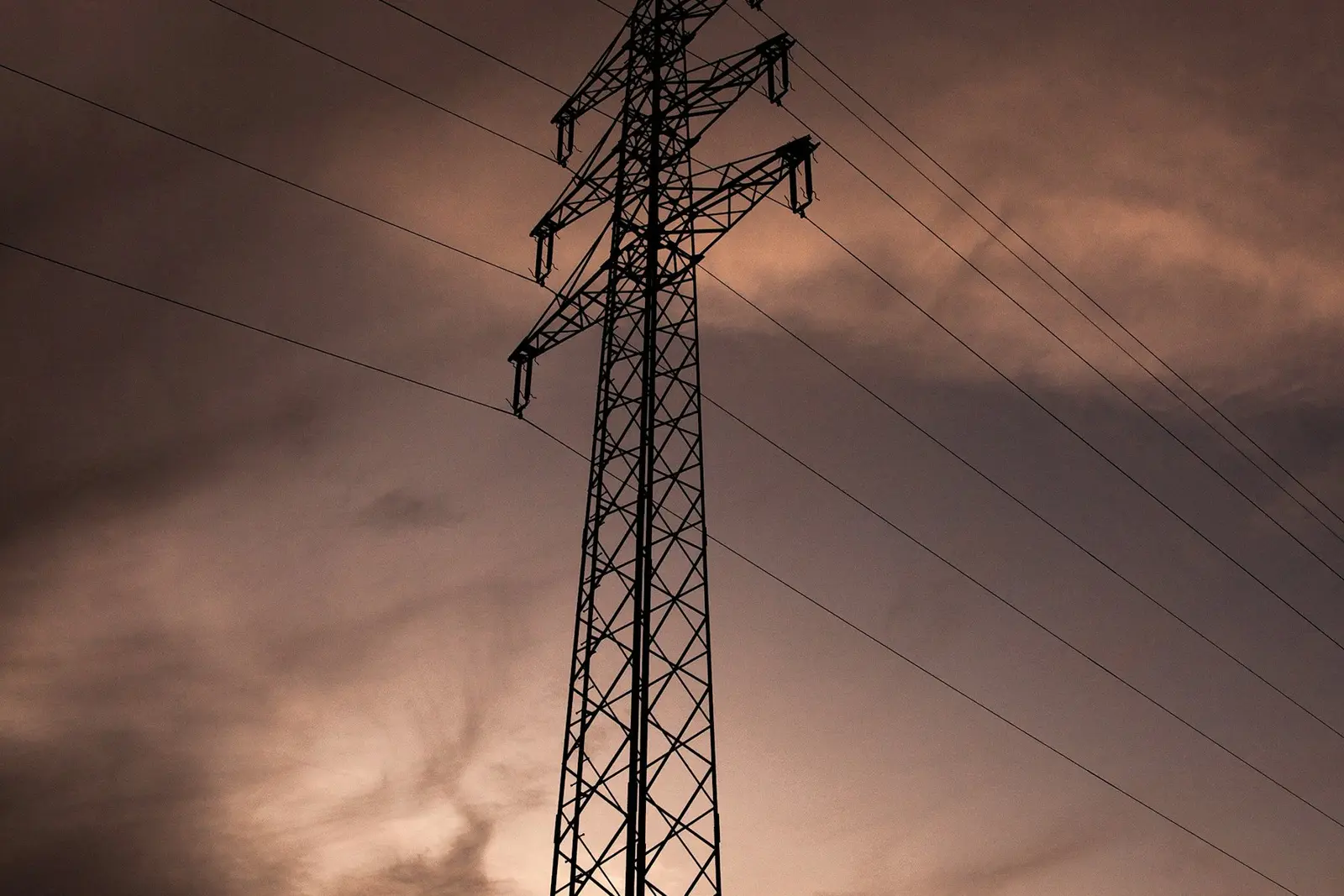 Een hoogspanningsmast met kabels tegen een donkere lucht bij zonsondergang